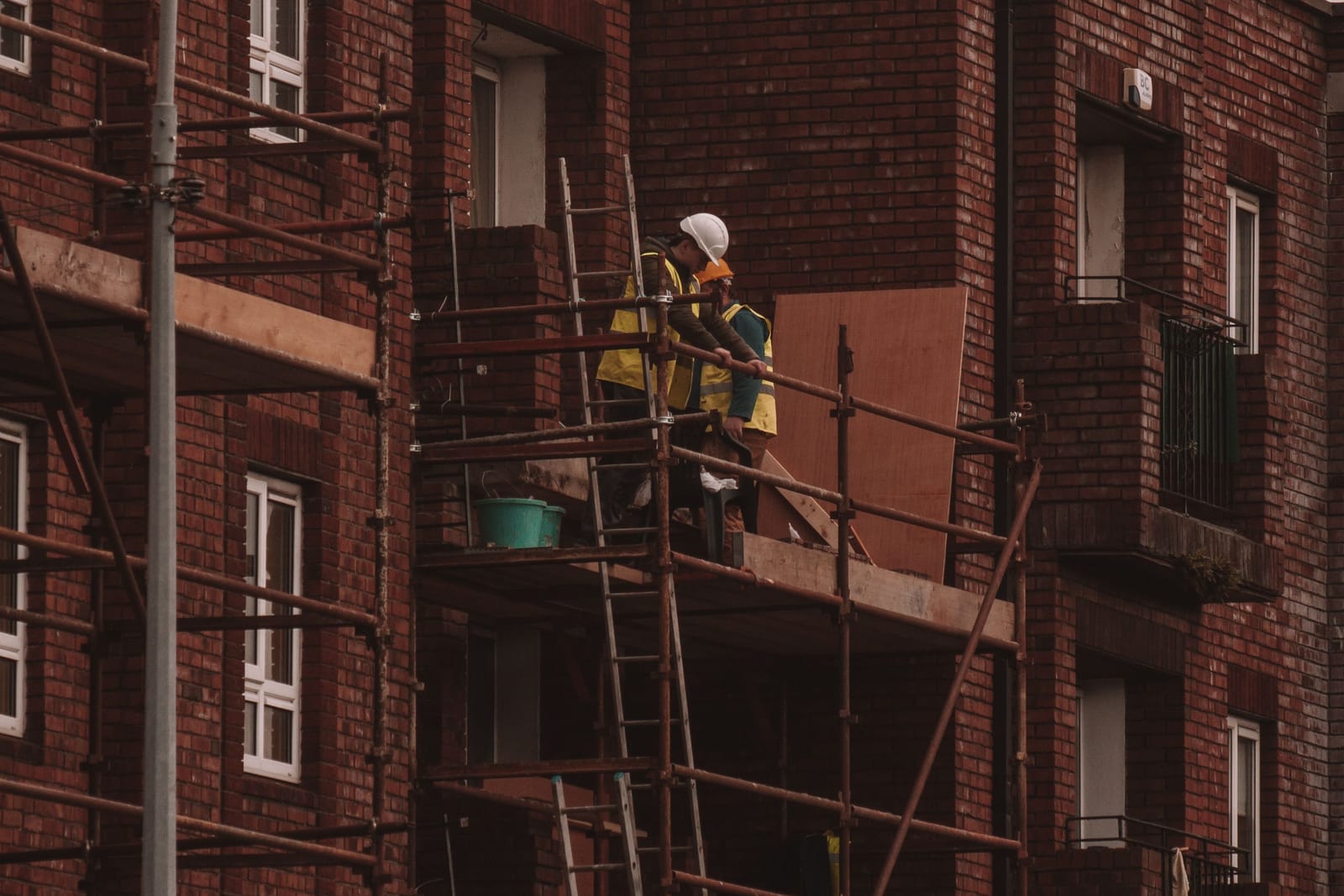 A builder in a hard hat and high-visibility vest on scaffolding against a red-brick building in Dublin